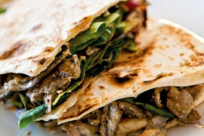 La Piadina con Saraghina, Radicchio e Cipolla è un piatto tipico della cucina romagnola, che unisce i sapori autentici della terra e del mare. La saraghina, piccolo pesce azzurro dalle note intense, viene grigliata e servita all’interno della tradizionale piadina romagnola IGP, insieme a radicchio croccante e cipolla caramellata, creando un perfetto equilibrio di sapori. Questo street food tipico di Rimini e della Riviera Romagnola è un'esperienza gastronomica imperdibile per chi desidera assaporare la vera tradizione locale.