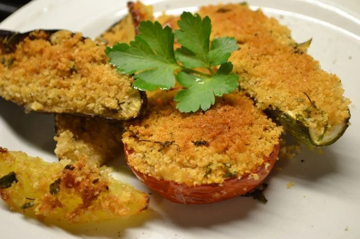 Le Verdure Gratinate alla Romagnola sono un contorno tradizionale della cucina romagnola, semplice ma ricco di sapore. Pomodori, zucchine, melanzane e patate vengono farciti con un mix di pangrattato, prezzemolo, aglio e olio extravergine d'oliva, poi cotti al forno fino a ottenere una deliziosa crosticina croccante. Questo piatto, chiamato anche "Verdure al Grattè", è perfetto per accompagnare secondi di carne o pesce, ed è una presenza immancabile nelle tavole di Rimini e della Romagna.