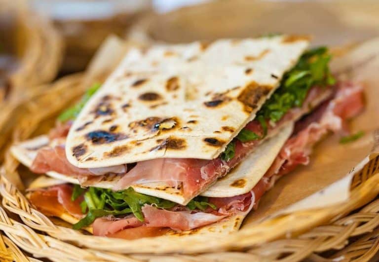 La Piadina Romagnola IGP è il simbolo della cucina tradizionale di Rimini e della Romagna. In questa immagine, la piadina è farcita con prosciutto crudo, rucola e squacquerone, un abbinamento classico che esalta i sapori autentici del territorio. Croccante fuori e morbida dentro, la piadina è perfetta per un pasto veloce, uno street food genuino o un’esperienza gastronomica da vivere nei chioschi tipici di Rimini.