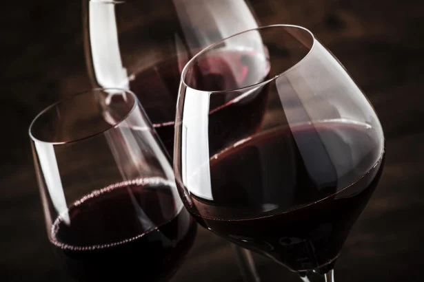 Dettaglio ravvicinato di tre calici ballon riempiti di vino rosso durante una degustazione professionale.