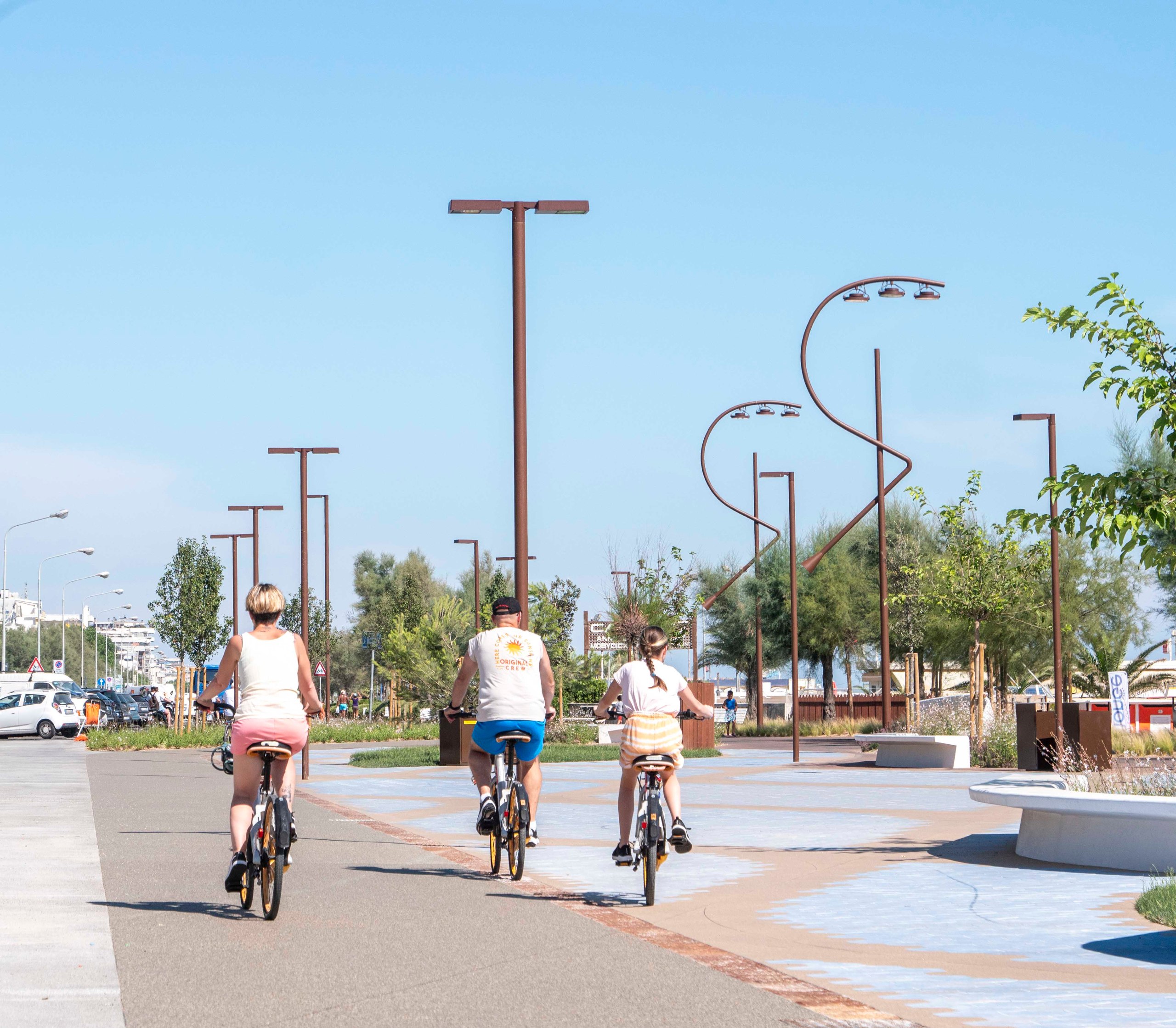 Tre ciclisti percorrono la pista ciclabile del Parco del Mare di Rimini con le lampade di design e il mare sullo sfondo